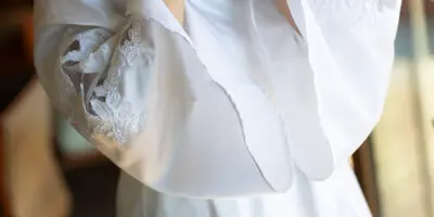 Bride in a white lace robe fastening an earring during wedding day preparations