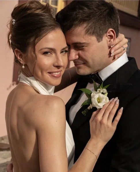 A bride with an elegant updo hairstyle and full makeup embracing a groom in a tuxedo.