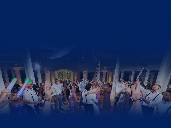 Wedding reception dance floor with guests dancing and holding glowing sticks under dim lighting.