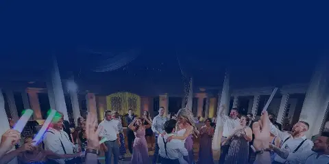 Wedding reception dance floor with guests dancing and holding glowing sticks under dim lighting.
