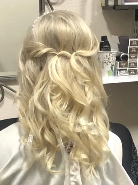 Back view of a client in a salon chair with a styled blonde half-up hairstyle.