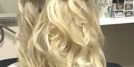 Back view of a client in a salon chair with a styled blonde half-up hairstyle.