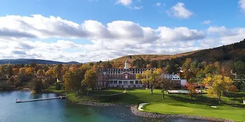 Aerial view of The Otesaga Resort Hotel on the shores of Otsego Lake with autumn foliage and a blue sky.