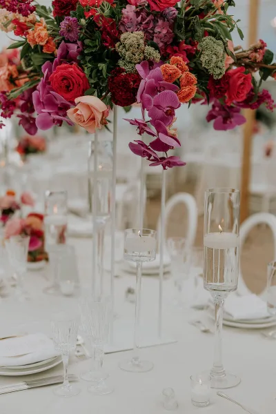 A tall, vibrant floral arrangement with red roses and purple orchids on a wedding reception table.