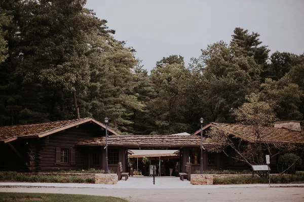 Exterior view of a historic log lodge building with a covered entrance, surrounded by tall pine trees.