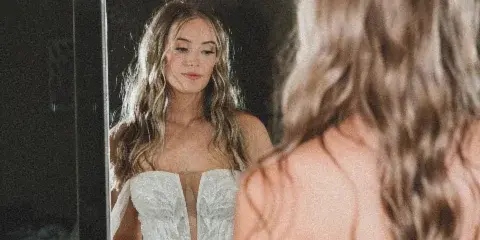 A bride in a white wedding dress looking at her reflection in a mirror.