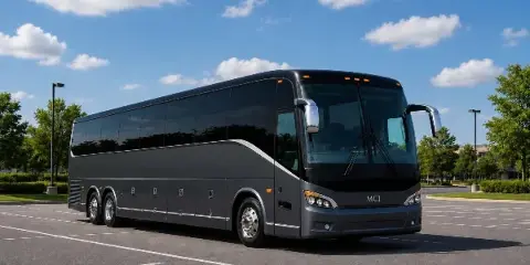 A large black charter bus parked in an empty parking lot under a blue sky with white clouds.