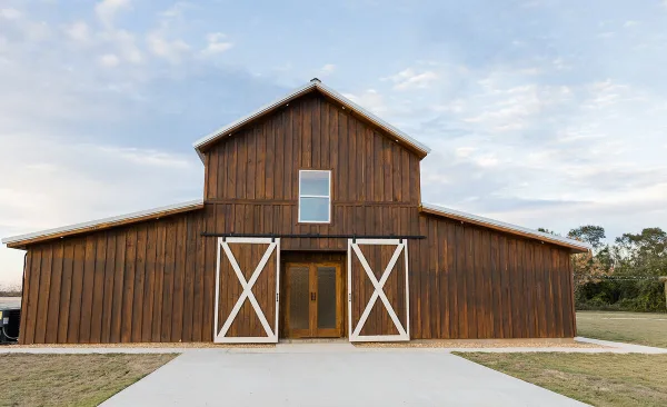 Exterior view of a large wooden barn with white barn doors and a concrete walkway leading to the entrance.
