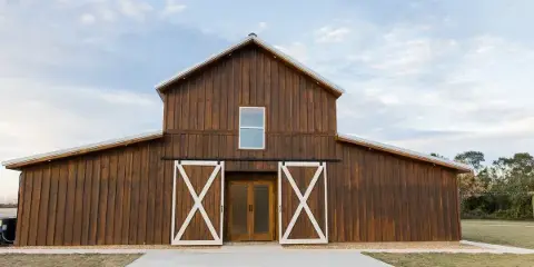 Exterior view of a large wooden barn with white barn doors and a concrete walkway leading to the entrance.