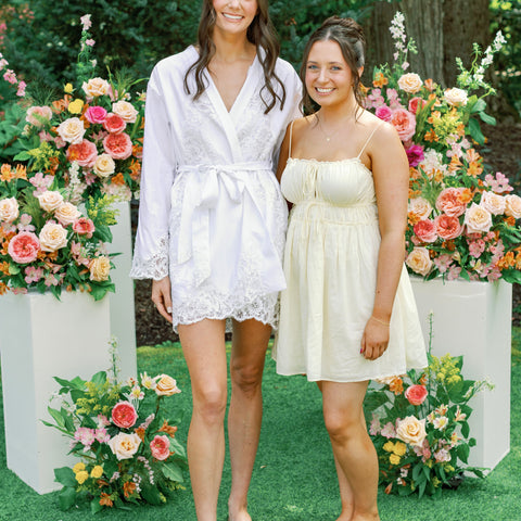 Two women standing in front of a wedding floral installation with large flower arrangements on white pedestals.