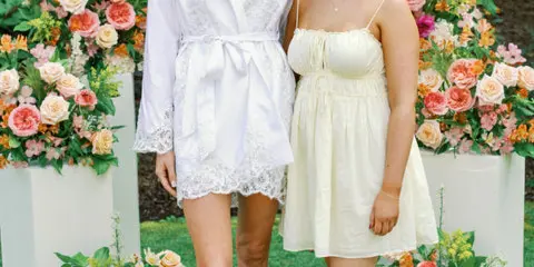 Two women standing in front of a wedding floral installation with large flower arrangements on white pedestals.