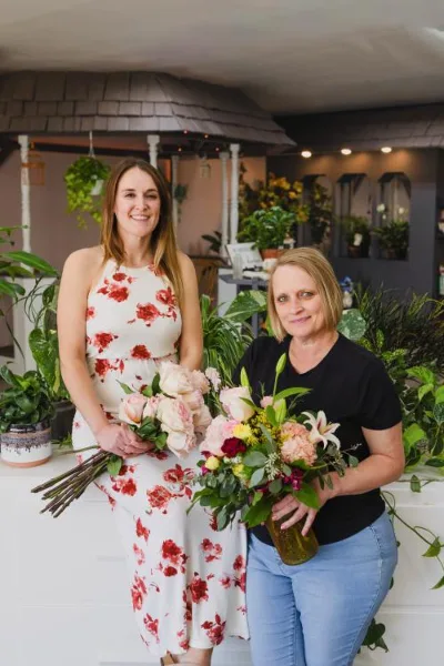Two women holding floral bouquets in a flower shop setting