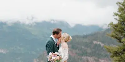 A bride and groom kissing in front of a mountain backdrop with floral arrangements.