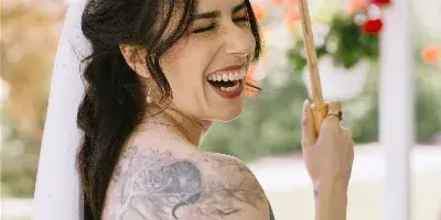 A smiling bride in a white lace dress and veil holding a paper parasol, with styled hair and makeup.