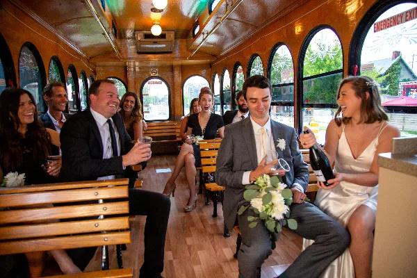 A bride and groom with their wedding party seated inside a vintage trolley.