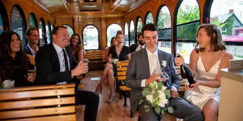 A bride and groom with their wedding party seated inside a vintage trolley.
