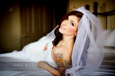 A bride with styled hair and makeup wearing a veil, seated on a bed.