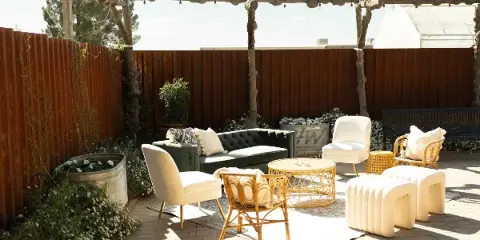 Rustic outdoor patio area featuring a wooden pergola, green sofa, white chairs, and potted plants.