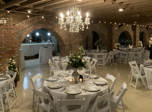 Indoor event venue with brick arches, exposed beams, and round tables set for a wedding reception.