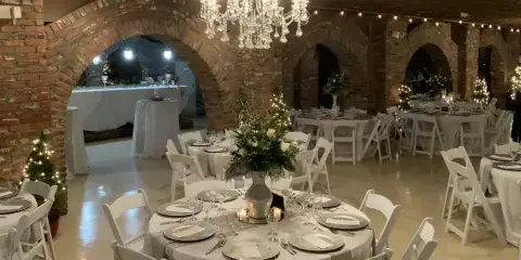 Indoor event venue with brick arches, exposed beams, and round tables set for a wedding reception.