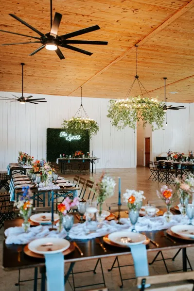 Interior view of a wedding reception hall with long farm tables, floral centerpieces, and a wooden ceiling.