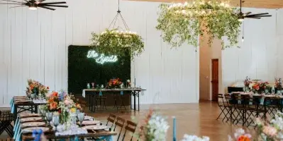 Interior view of a wedding reception hall with long farm tables, floral centerpieces, and a wooden ceiling.