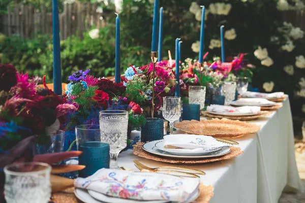 A close-up view of a wedding table setting featuring white plates, gold flatware, crystal glassware, blue candle holders, and a vibrant floral centerpiece.