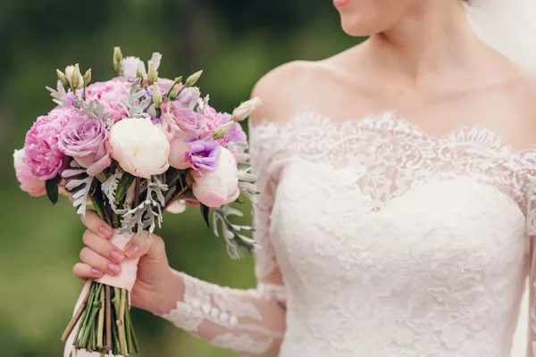 A bride in a white lace wedding dress holding a bouquet of pink and white flowers.