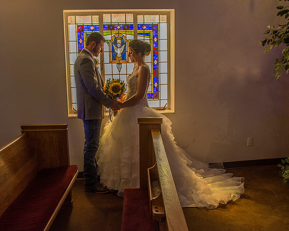 A bride and groom standing in a church aisle in front of a stained glass window.