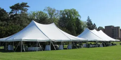 Large white frame tents set up on a grassy lawn with tables and chairs underneath.