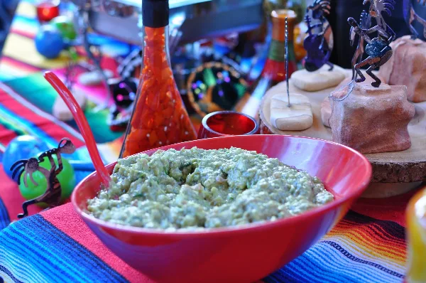 Bowl of fresh guacamole on a colorful Mexican-style catering table with salsa and decorative items