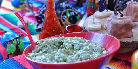Bowl of fresh guacamole on a colorful Mexican-style catering table with salsa and decorative items