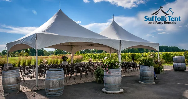 Outdoor event setup featuring a large white tent, rows of chairs, and decorative wooden barrels.