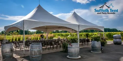 Outdoor event setup featuring a large white tent, rows of chairs, and decorative wooden barrels.