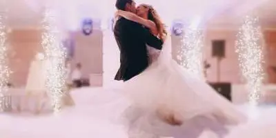 A bride and groom dancing at a wedding reception with string lights in the background.