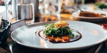 A plated food dish with garnish being served at a dining table.