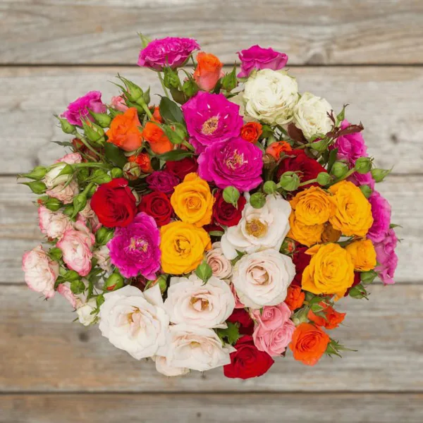 A colorful floral bouquet featuring roses and carnations in shades of pink, red, orange, yellow, and white, arranged on a rustic wooden surface.