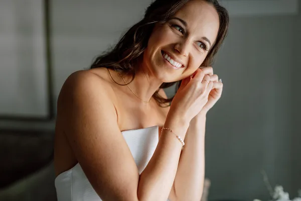 A smiling bride with styled hair and makeup wearing a white strapless dress.