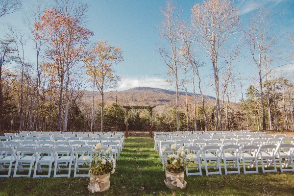 Outdoor wedding ceremony site with white chairs and a wooden arbor set against a mountain landscape.