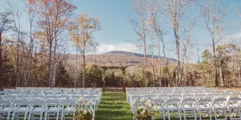 Outdoor wedding ceremony site with white chairs and a wooden arbor set against a mountain landscape.