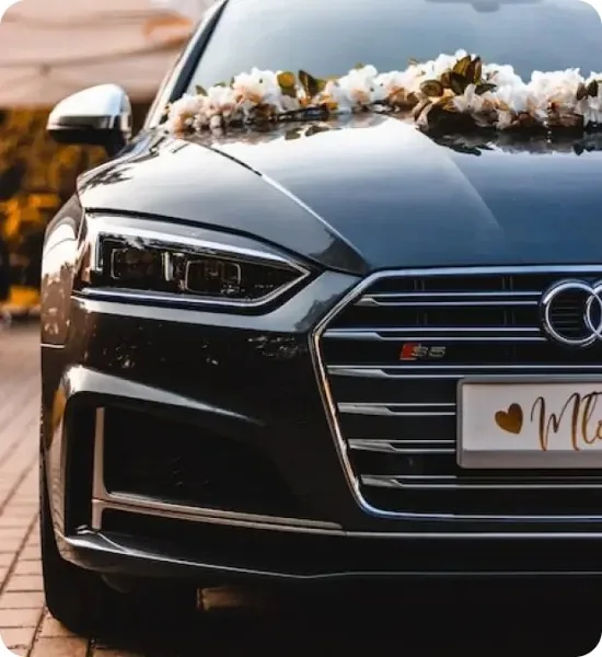 Front view of a black luxury sedan decorated with a white floral garland and a 'Mr' license plate frame.