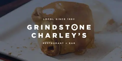 A plated food item, appearing to be a pastry or dessert, on a white square plate with the text 'Grindstone Charley's Restaurant + Bar' overlaid.