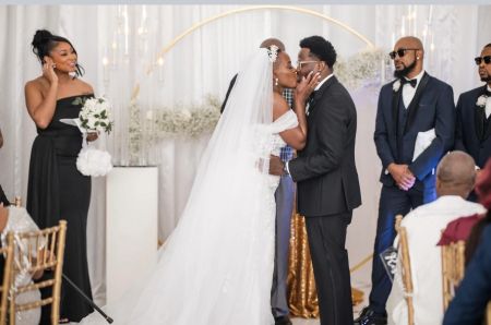 Bride and groom sharing a kiss during a wedding ceremony at an indoor venue with a floral arch and seated guests.