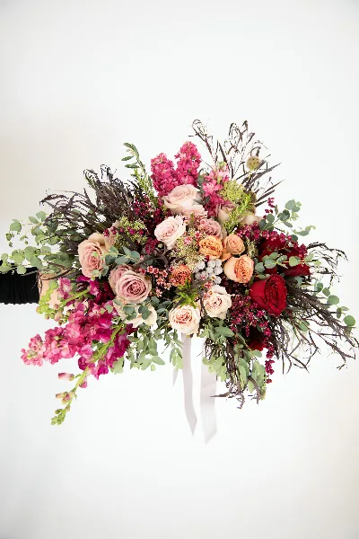 A cascading wedding bouquet with pink and red roses, magenta stock, and eucalyptus held against a white background.