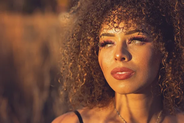 Natural light portrait of a woman with curly hair in warm outdoor lighting.