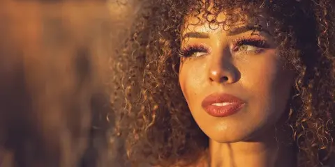 Natural light portrait of a woman with curly hair in warm outdoor lighting.