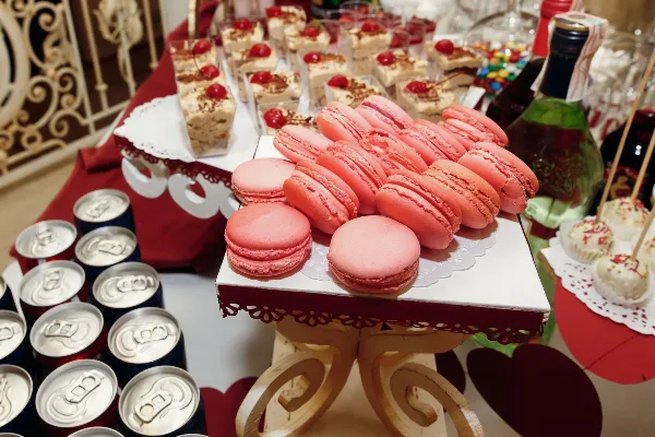 A catering dessert table featuring pink macarons, tiramisu cups, and cake pops arranged on a decorated stand.