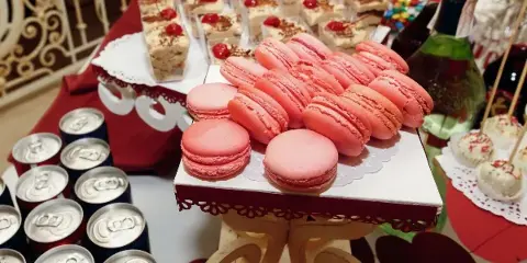 A catering dessert table featuring pink macarons, tiramisu cups, and cake pops arranged on a decorated stand.