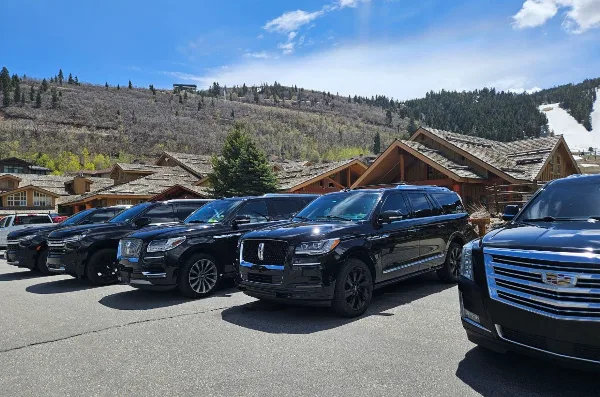 A row of black luxury SUVs parked in a lot with a mountain resort in the background.