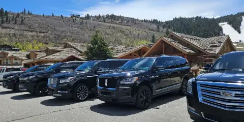 A row of black luxury SUVs parked in a lot with a mountain resort in the background.